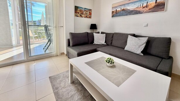 Un saló modern amb un sofà gris, una taula de centre blanca i una porta de vidre que dona a una zona exterior.