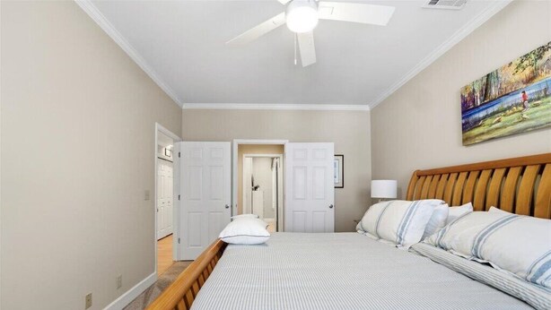 A bedroom with a bed, a ceiling fan, a painting on the wall, and a door leading to another room.