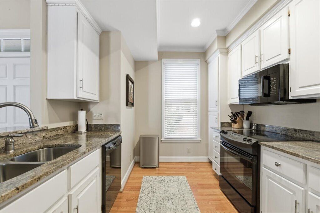 A kitchen with white cabinets, a granite countertop, a stainless steel sink, a black microwave, and a stainless steel range hood.