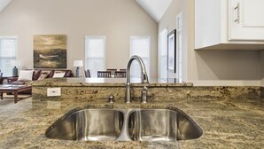 A kitchen with a double sink, a ceiling fan, and a painting on the wall.