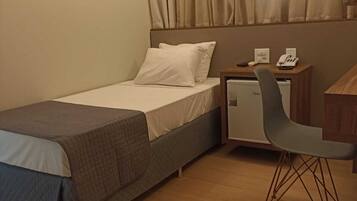 A hotel room with a bed, a desk with a chair, a nightstand, and a wall-mounted lamp.