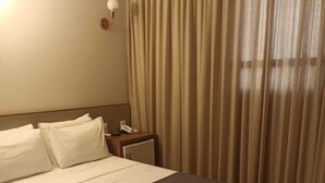A hotel room with a large bed, a bedside table with a lamp, and a window with curtains.