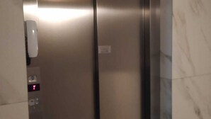 A modern elevator with a metallic finish, a control panel with buttons, and a marble wall.