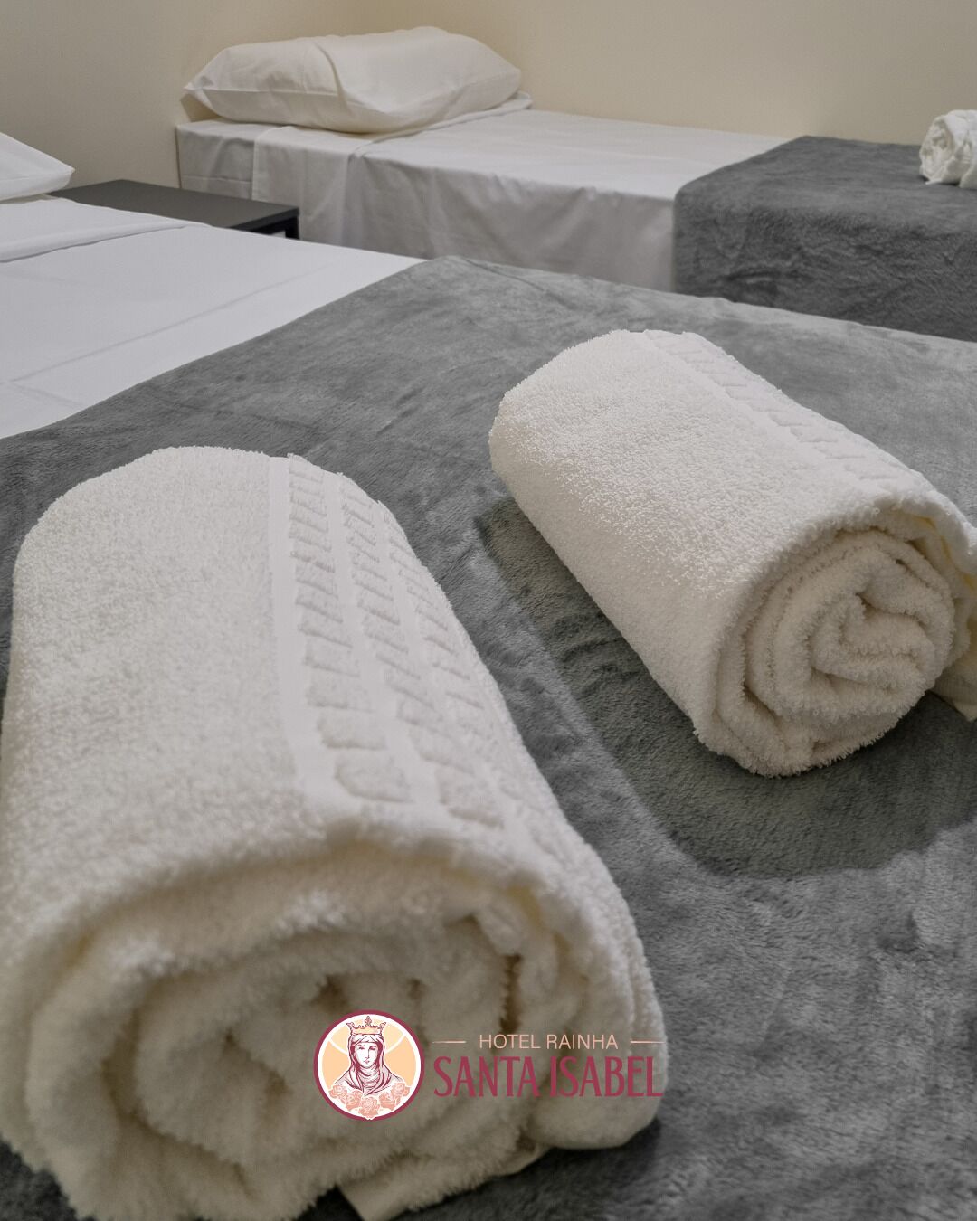 Habitació d'hotel amb dos llits, cadascun amb roba blanca i una manta gris.