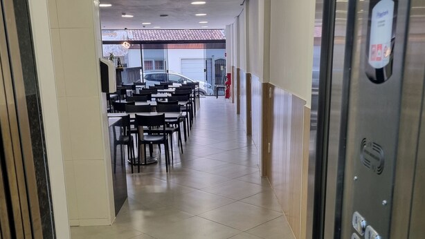 Un couloir au sol carrelé, une rangée de tables et de chaises, et un ascenseur sur le côté droit.