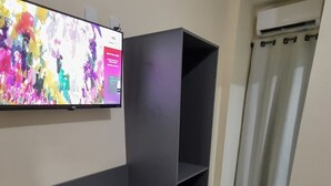 Une pièce avec un canapé gris, un téléviseur à écran plat fixé au mur et un petit appareil blanc posé sur le sol.