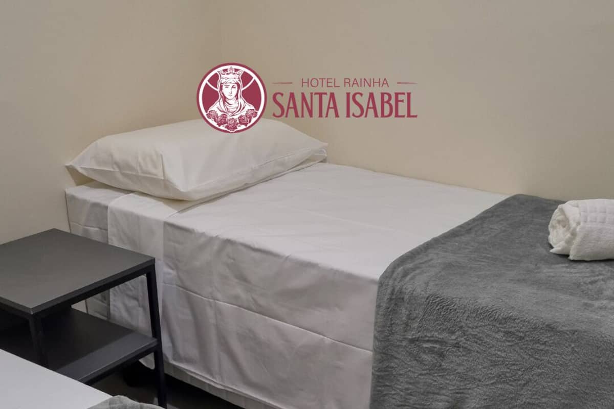Hotellihuone, jossa on sänky, pieni pöytä ja harmaa peitto.