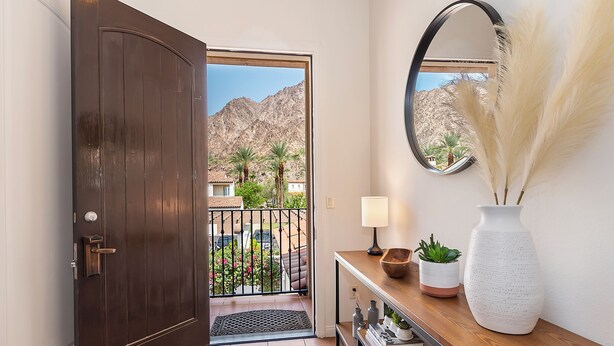 Una puerta de madera oscura que da a un balcón con vistas a montañas y palmeras.