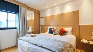 A hotel room with a large bed, a bedside table with a phone, a window with curtains, and a view of the city.