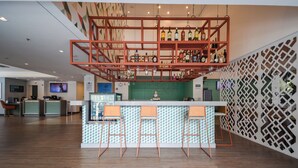 A modern bar area with a high ceiling, wooden floor, and a bar counter with stools.