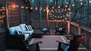 A wooden deck with outdoor seating, string lights, and a view of the forest. - White-Tail Nook Blue Ridge Cabin! (Blue Ridge)