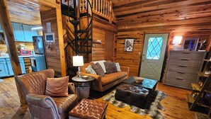 A cozy cabin interior with a wooden staircase, a living area with a sofa, a leather armchair, and a coffee table. - White-Tail Nook Blue Ridge Cabin! (Blue Ridge)
