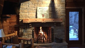 Ein gemütliches Holzblockhaus-Interieur mit Kamin aus Stein, Holzmöbeln und einem an der Wand befestigten Fernseher.