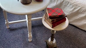 A cozy room with a white sofa, a small round table with a vase of flowers, two cups, and a stack of books.