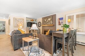 A living room with a sofa, a coffee table, a dining table with chairs, a TV, and a fireplace.
