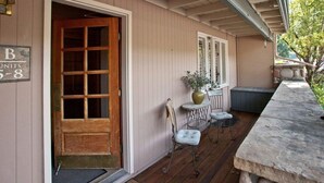 A wooden porch with a door, a small table with chairs, and a potted plant.