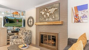 A living room with a fireplace, a television, a world map artwork, and a ski-themed poster.