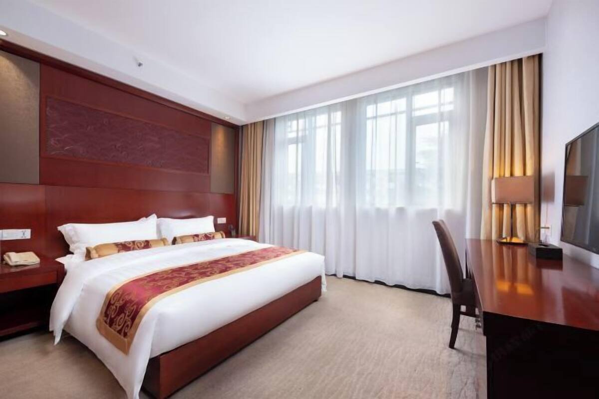 Hotellihuone, jossa on suuri sänky, työpöytä, tuoli, televisio ja ikkuna, jossa on verhot.