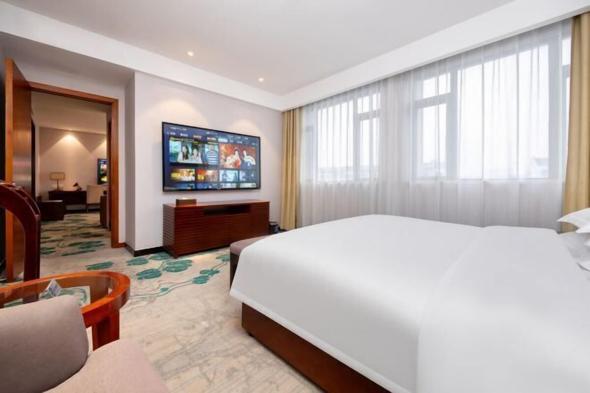 A hotel room with a large bed, a TV mounted on the wall, a wooden desk, and a chair.