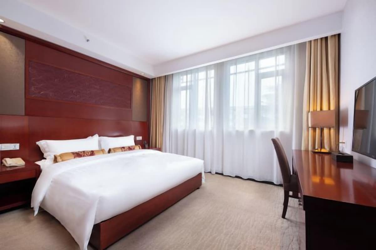 A hotel room with a large bed, a desk, a chair, a TV, and a window with curtains.