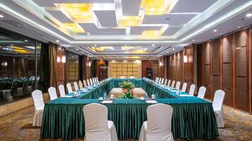 A conference room with a long table, white chairs, and a green tablecloth.