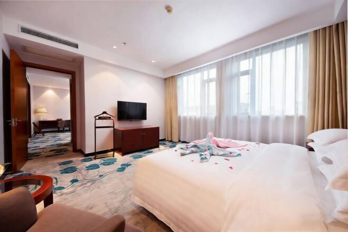 Hotellihuone, jossa on suuri sänky, televisio, työpöytä ja tuoli.