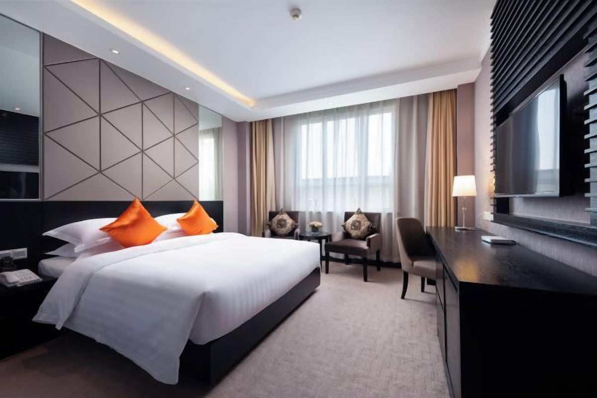 A modern hotel room with a large bed, a desk, a chair, and a TV.