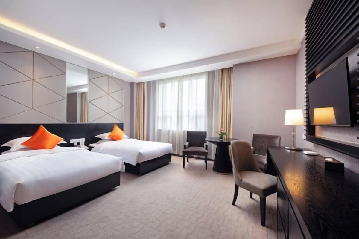 A hotel room with two beds, a desk, a chair, a lamp, and a large mirror.