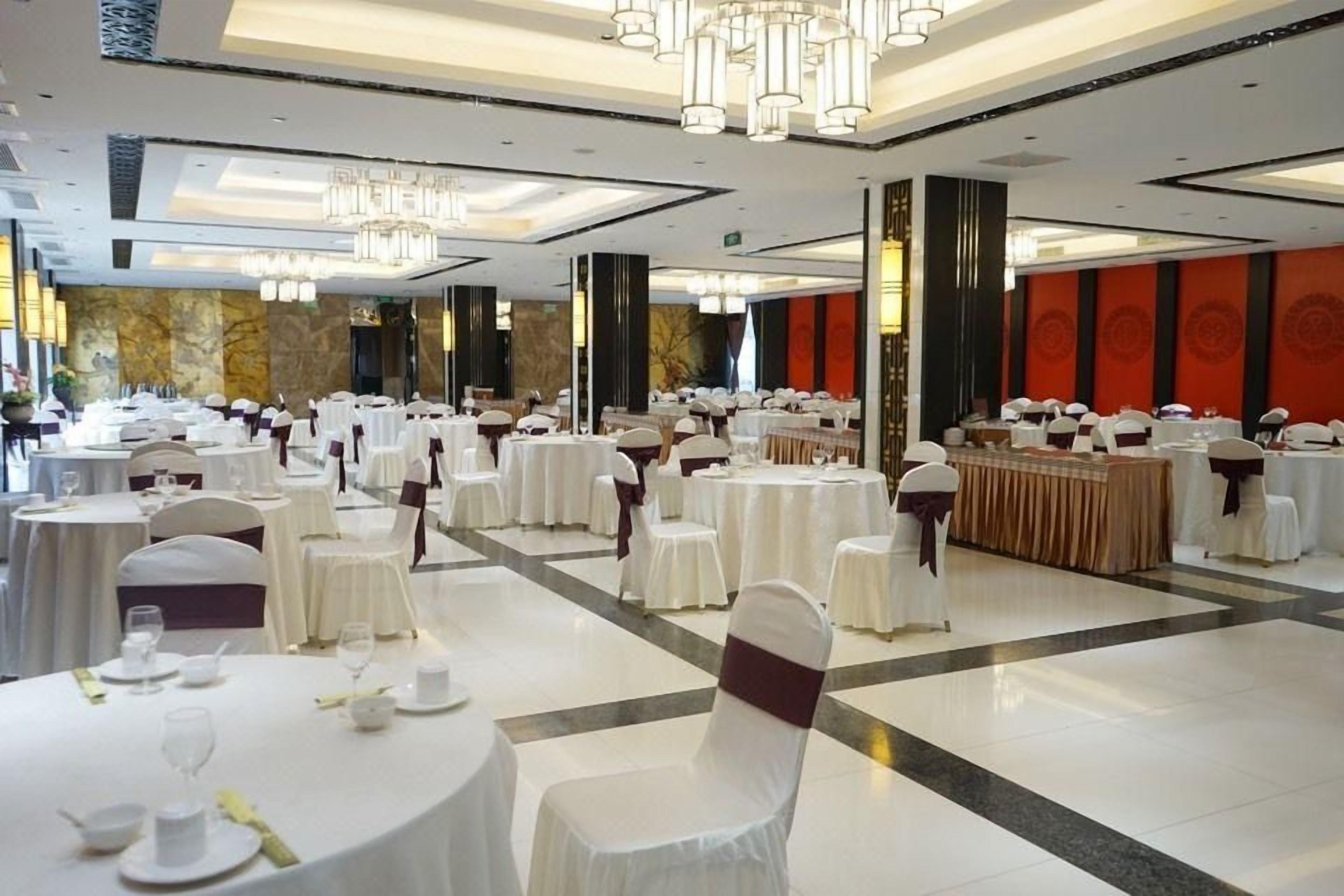 A banquet hall with round tables, chairs, and a central buffet area.