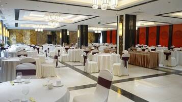 A banquet hall with round tables, chairs, and a central buffet area.