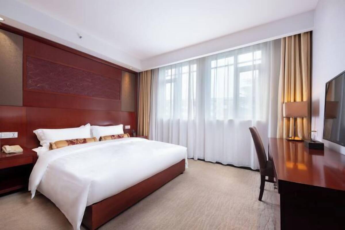 Hotellihuone, jossa on suuri sänky, työpöytä, tuoli, televisio ja ikkuna, jossa on verhot.