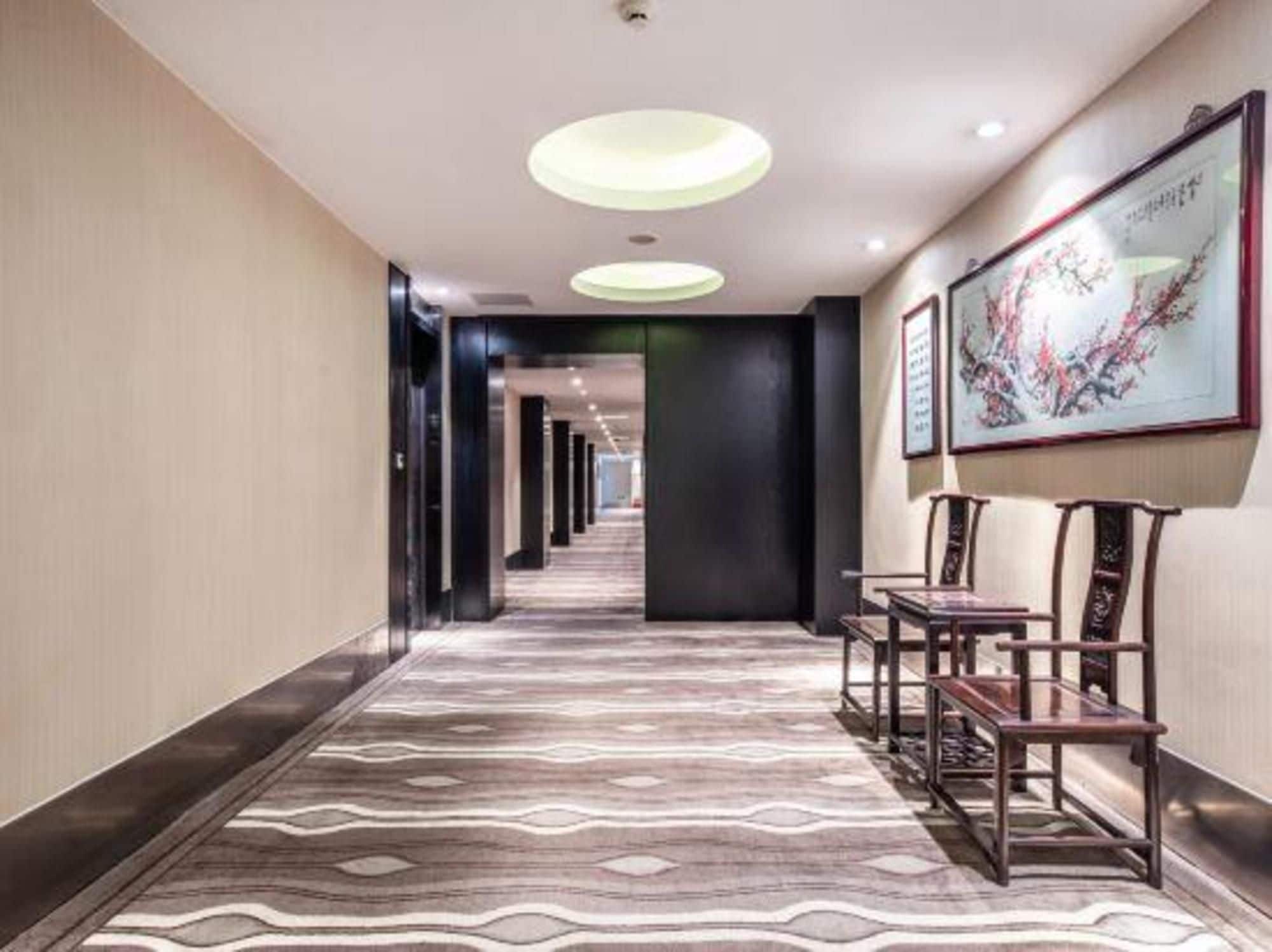 A hotel hallway with a patterned carpet, a row of chairs, and framed artwork on the wall.