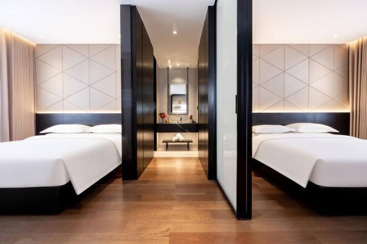 Hotellihuone, jossa on kaksi sänkyä, penkki, peili ja pieni pöytä.