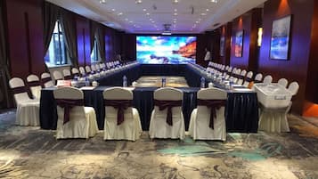 A conference room with a long table, chairs, and a large screen at the front.