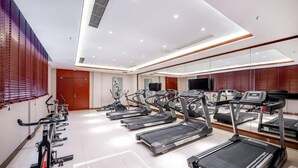 A gym with multiple treadmills and exercise bikes, a large mirror, and a television on the wall. - Xiangxuehai Hotel (Suzhou)