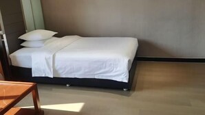 Una cama bien hecha con ropa blanca en una habitación con suelo de madera y pared lisa.