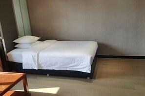 A neatly made bed with white bedding in a room with a wooden floor and a plain wall.