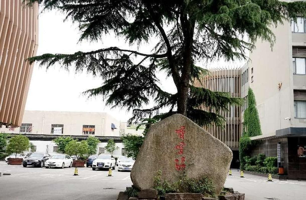 A stone monument with Chinese characters, a parking lot with cars, and a modern building with a glass facade.