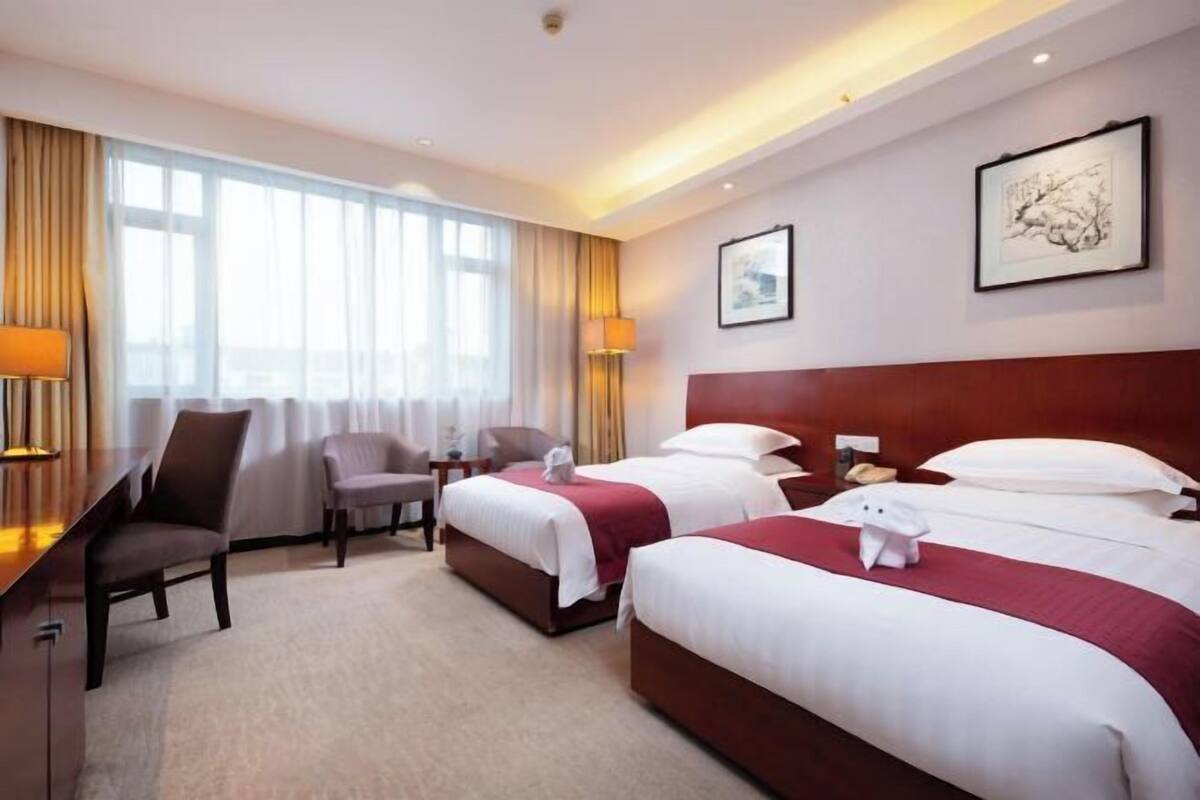 Hotellihuone, jossa on kaksi sänkyä, työpöytä, tuoli ja suuri ikkuna.
