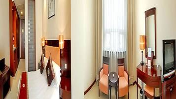 A hotel room with a bed, a desk with a television, a chair, and a small table.