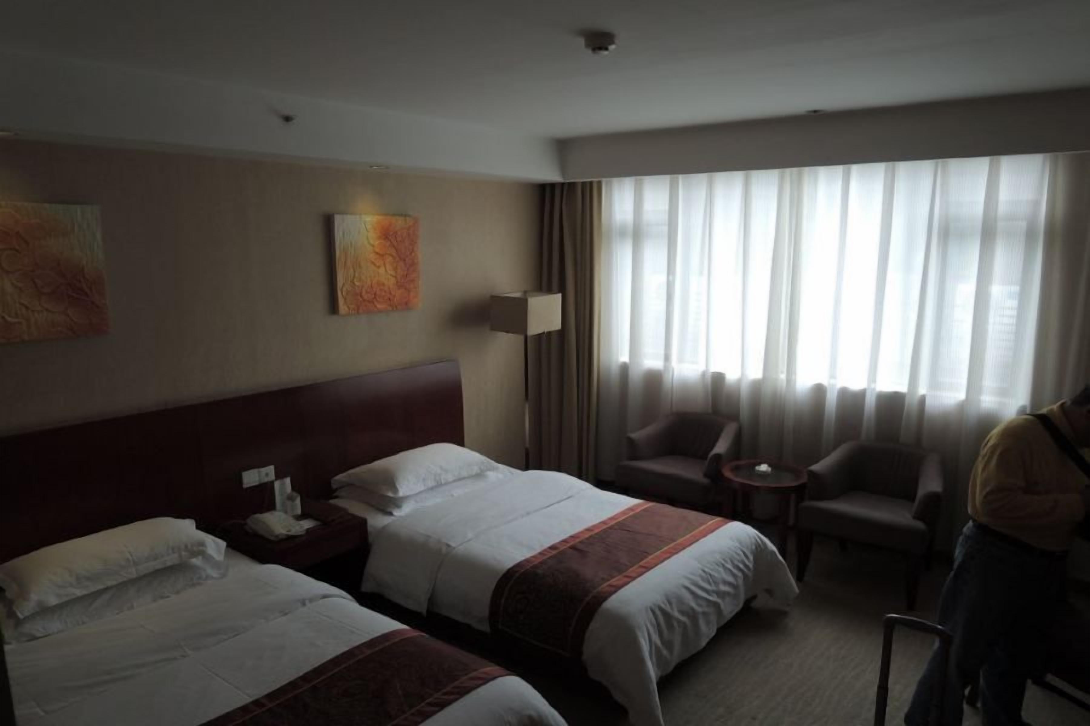 A hotel room with two beds, a sitting area with a chair, a lamp, and artwork on the wall.