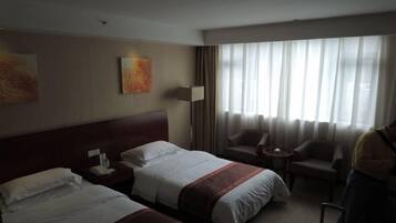 A hotel room with two beds, a sitting area with a chair, a lamp, and artwork on the wall.