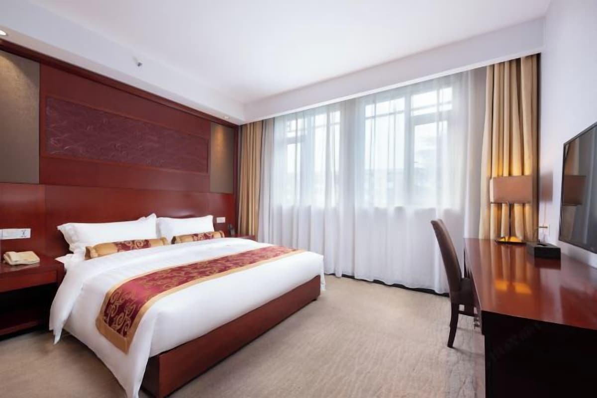 A hotel room with a large bed, a desk, a chair, a TV, and a window with curtains.