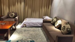 Una habitación con un sofá, una silla, una mesita y una cama con colcha estampada.