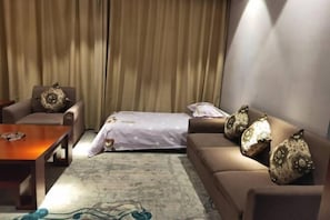 A room with a sofa, a chair, a small table, and a bed with a patterned bedspread.