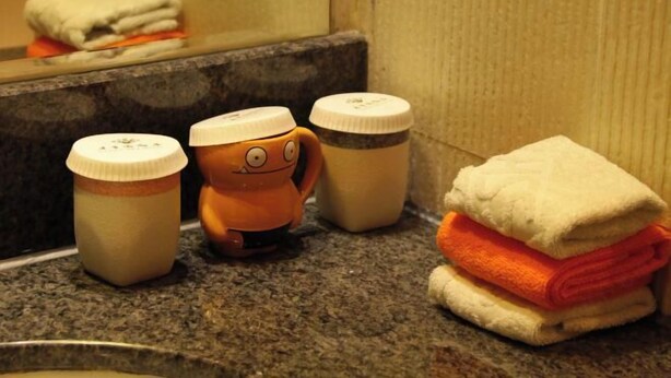 Una encimera de baño con una pila de toallas, un juguete naranja pequeño y dos botellas.