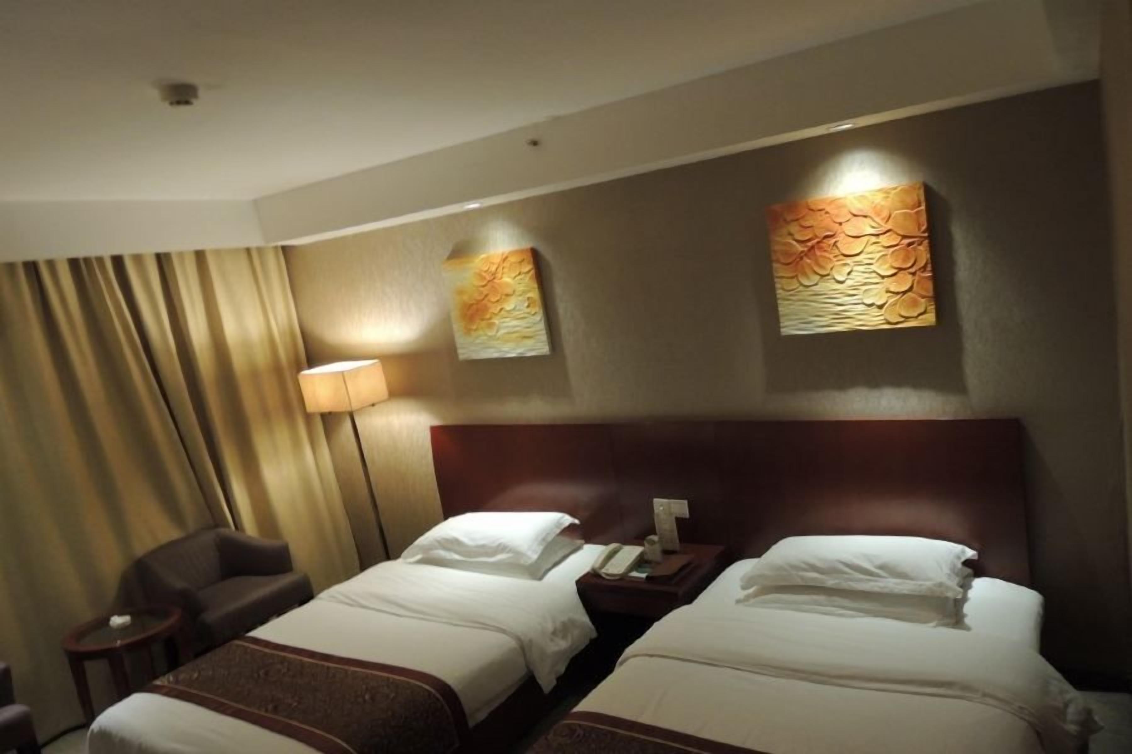 A hotel room with two beds, a nightstand, a lamp, and a chair.