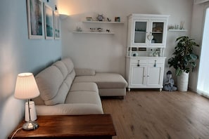 Un salon comprenant un canapé, une table d’appoint en bois, une lampe, un meuble et une plante en pot.