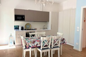 A compact kitchen with a microwave, stove, and sink, a dining table with chairs, and a chandelier.