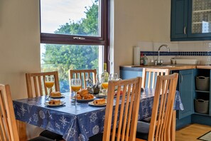 A dining table with a nautical-themed tablecloth, wooden chairs, and breakfast items including croissants and orange juice. - Cottage in Cornwall With Stunning Sea Views (Penzance)